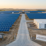 A wide aerial view of a massive utility-scale solar power plant featuring Ampt’s string-level optimizers integrated with a DC-coupled battery energy storage system (BESS). The image showcases a modern infrastructure with white battery containers and rows of PV panels, illustrating how Ampt lowers LCOE and improves round-trip efficiency for large-scale solar-plus-storage projects.